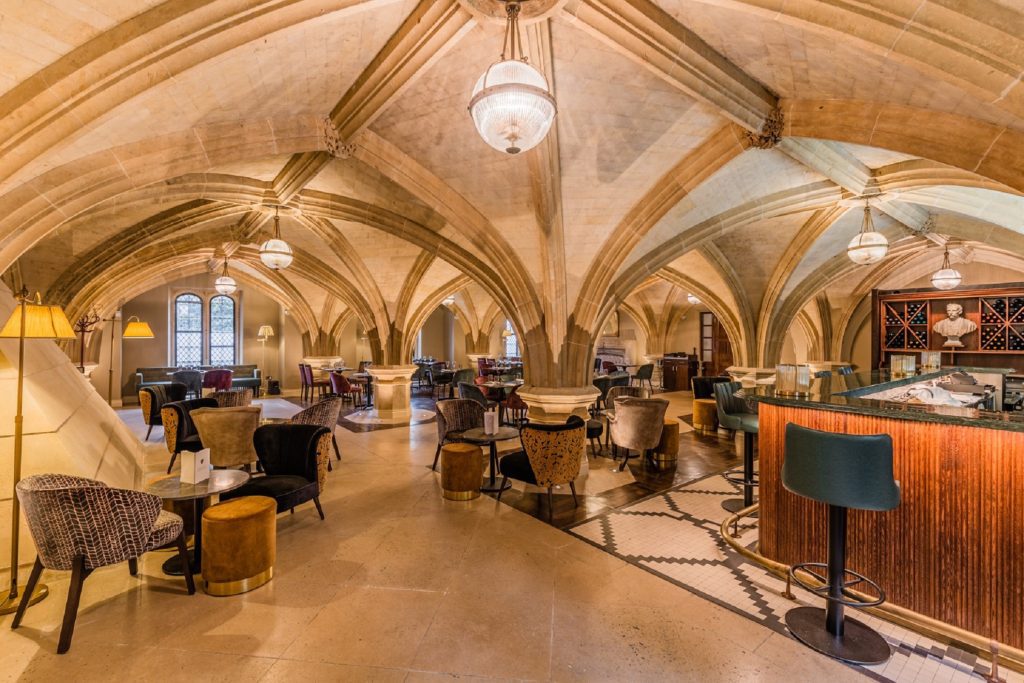 Tables set up for dinner in restaurant with domed ceilings and chandeliers with bar at the side and large windows letting in natural light